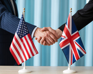 Two business people shaking hands with American and British flags on a table, symbolizing international partnership and diplomacy.