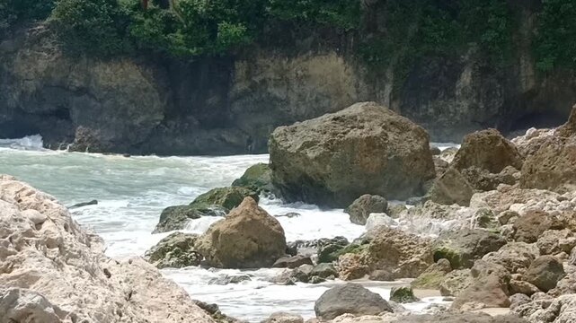 Strong waves at Sawangan Beach crash hard against the large coastal rocks, creating a burst of white spray as the current grows stronger. The impact shows the powerful and dynamic nature.