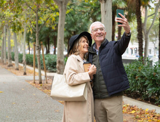 Happy senior couple enjoying autumn walk and taking a selfie with copy space