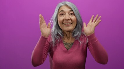 Senior woman with grey hair joyfully playing peekaboo against a vibrant pink wall, showing expressions of surprise and delight.