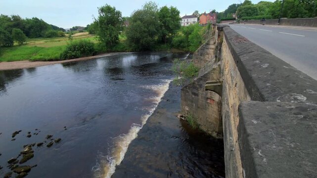 Wide shot of River Ure spilling over low weir next to road bridge in Ripon