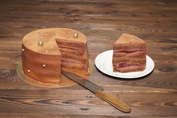 A confectionery product. A chocolate cake with a cut-out slice on a golden base, on a wooden table.