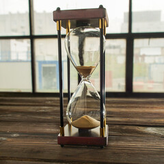 Hourglass on a wooden table against a window. Hourglass as a symbol of time. The concept of time passing irrevocably.