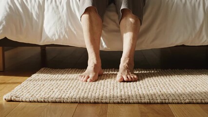 An older person's bare feet touching a rug when getting out of bed. Senior waking up in a sunlit bedroom. Morning routine and aging concept