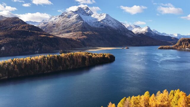 Snow-capped alpine mountains with golden larch forest and pristine blue lake waters.