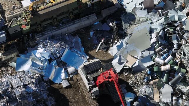 Working Excavator on scrapyard in industrial area of town. Aerial top down flyover. Sunny day. steel and aluminum on junkyard.