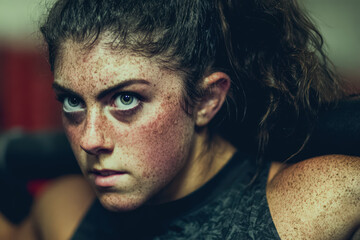 Determined female athlete with freckles performing weightlifting squat in gym, intense focused expression and muscular shoulders