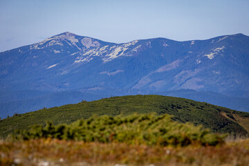Distant rugged mountains with pale rock patches rise beyond a rolling green ridge, and alpine...
