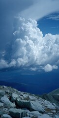 Majestic cumulonimbus clouds dominate a vast blue sky above a rugged rocky mountain summit overlooking a distant valley