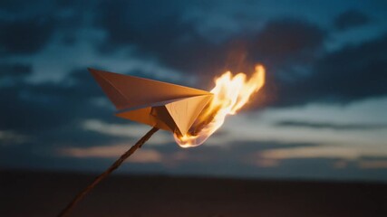 A burning paper plane on a stick at dusk, a metaphor for passion, failure, or a final message