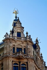 Fototapeta premium Ornate historic building facade featuring a golden angel statue with lightning bolts against a clear blue sky. Antwerp, Belgium