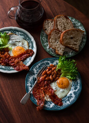 Breakfast table - fried egg with bacon and beans in tomato sauce on a wooden table, top view