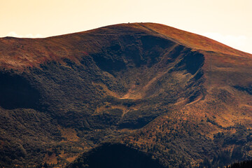 Naklejka premium Sunlit alpine cirque on a rounded mountain summit, showing dramatic bowl-shaped erosion, warm autumn tones, and textured slopes. Ideal for travel, geology and nature background or editorial uses.