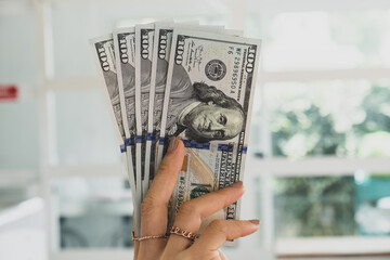 US dollars money 10 domination note on hand showing above a head the airport background. US dollars or American dollars currency with warm light.