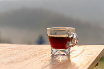 Glass cup of black coffee on wooden table with soft morning light and blurred outdoor background