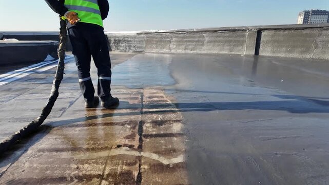A construction worker sprays insulation foam on a roof to improve thermal protection and energy efficiency.