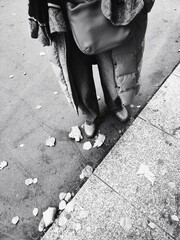 Standing on a Leaf-Littered Sidewalk. A person stands on a sidewalk covered with fallen leaves. The image captures the lower half of the figure wearing jeans and a long coat.