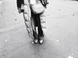 Street Style in Black and White. A person wearing a long puffer coat stands alone on a street, capturing a moment of everyday urban fashion. The monochrome palette adds a timeless feel.