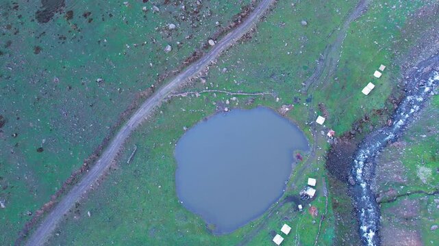 Top-down aerial of Chinar Lake beside stream and tents in lush Surgan Valley. Azad Kashmir, Pakistan
