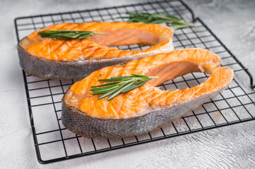 Two cooked salmon slices with herbs resting on a metal grid against a soft gray surface for fresh clean modern food styling.