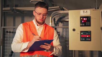Professional diligently records data from an industrial control panel. Focused worker maintains factory equipment, ensuring efficient and safe operations. Shows serious concentration.