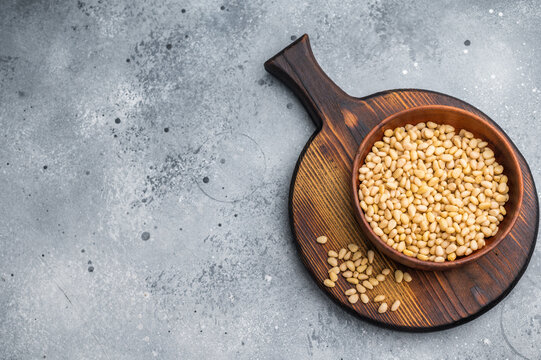 Close view of raw pine nuts in a rustic wooden bowl on a bright white backdrop giving a clean organic feel suitable for culinary and healthy food themes