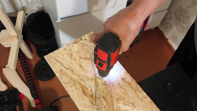 A man holds Power drills in his hand and screws into a wooden OSB board. Repair, assembly of furniture, construction. top view