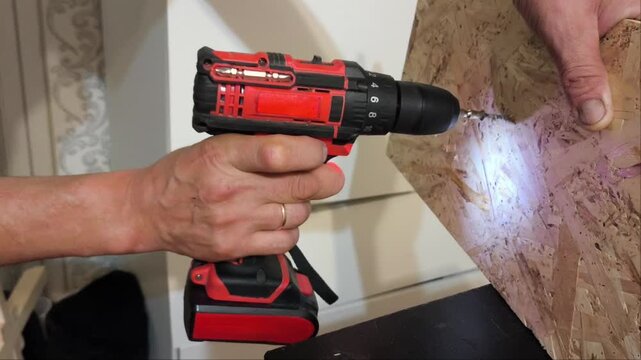 A man's hand uses Power drills to drive metal screws into an OSB panel. Renovation process in the apartment.