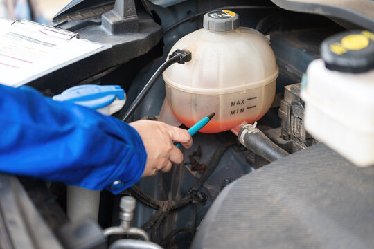Action of a car service technician is checking radiator coolant fluid level in the tank bottle. Car maintenance scene, close-up with selective focus.