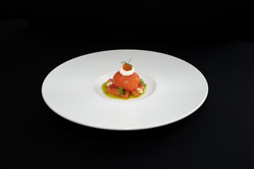 A beautifully plated gourmet appetizer against a dark background, showcasing culinary art. A single portion sits gracefully on a white plate