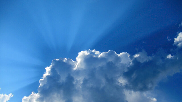 Blue sky with storm clouds and sunbeams breaking through them.