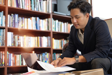 Businessman analyzing documents in cozy library with laptop, reflecting study, research, remote work, knowledge planning educational productivity.