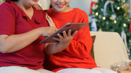 Joyful Connection. Two women sharing a tablet and laughter in a festive setting.