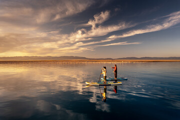 Two girls stand on standup paddle sup boards on lake in summer and enjoy sunset. Aerial view of sup surfers. Mongolia