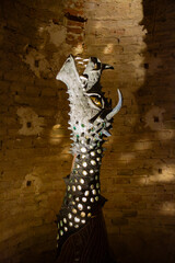 A dramatic abstract sculpture of a mythical dragon head with glowing elements stands against an ancient brick wall