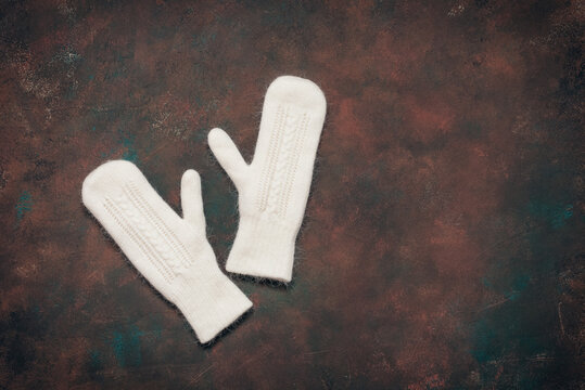 White fluffy knitted mittens on dark grunge background, top view, flat lay