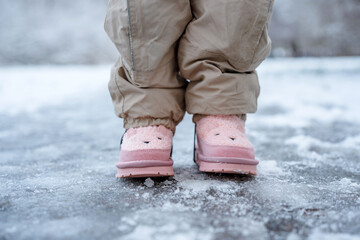 A child's feet in cute pink boots on a snowy path in winter