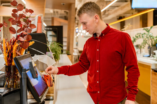 A young man chooses something at the checkout in a cafe