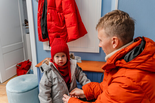 The father helps the little child girl get dressed, the father buttons his daughter's winter jacket at home