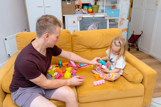 A young father and daughter little child play construction kit together on the couch in the children's room