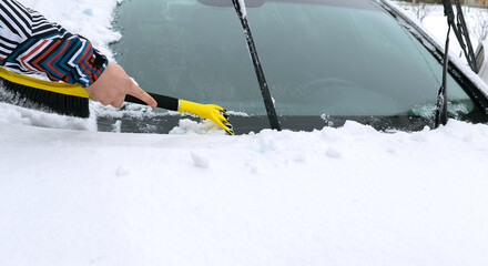 Man brushing snow and ice from windscreen of car with brush. Person cleaning fresh snow after snowstorm from car in the winter