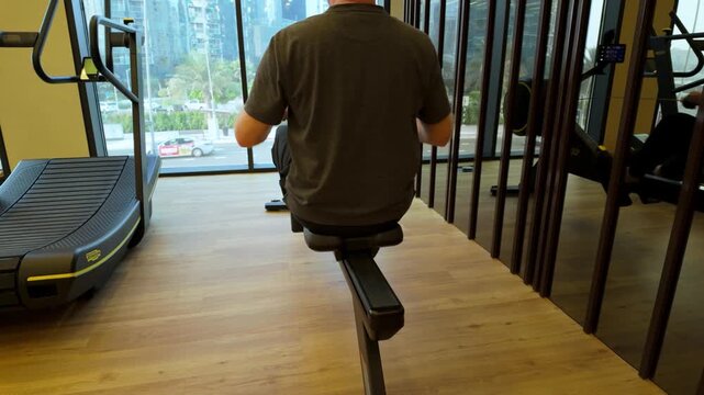 Behind Shot Of A Man Working Out In A Indoor Gymnasium On A Rowing Machine For Health And Wellbeing.