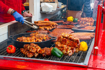 Grilled skewers and sausages at Christmas market, hot meats, peppers and festive street food prepared fresh at a holiday food stall
