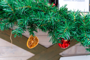 Christmas garland with green branches, dried orange slice and red bauble at holiday market creating natural decorative festive winter atmosphere