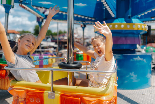 Two girls waving and having fun on a carousel ride at amusement park