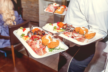 Professional waiter serving appetizer plates with prosciutto and croquettes at catering event