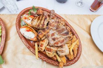 Hearty assortment of grilled meats, fries, and stuffed peppers served on a decorative platter during a festive meal