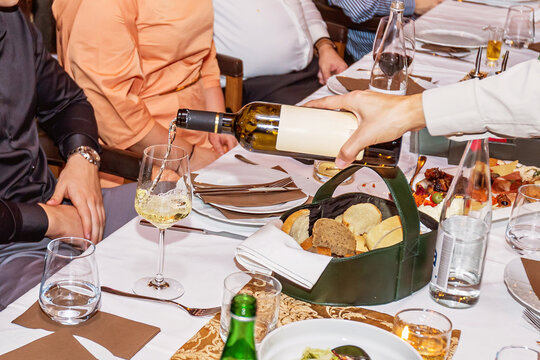 Waiter pouring white wine into glass at upscale formal dinner restaurant