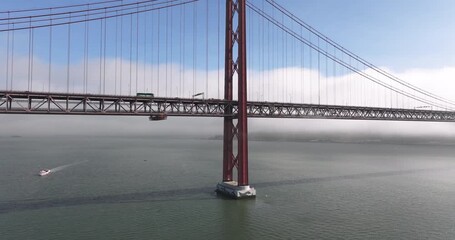 Aerial drone shot towards the 25th April Bridge in Lisbon, Portugal, Europe. Sunny and bright with clouds, fog, mist, covering the bridge. Central supporting column close-up