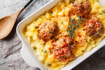 Baked beef meatballs with mashed potatoes, cheddar, tomato sauce, and thyme in a baking dish on the table. Horizontal top view from above